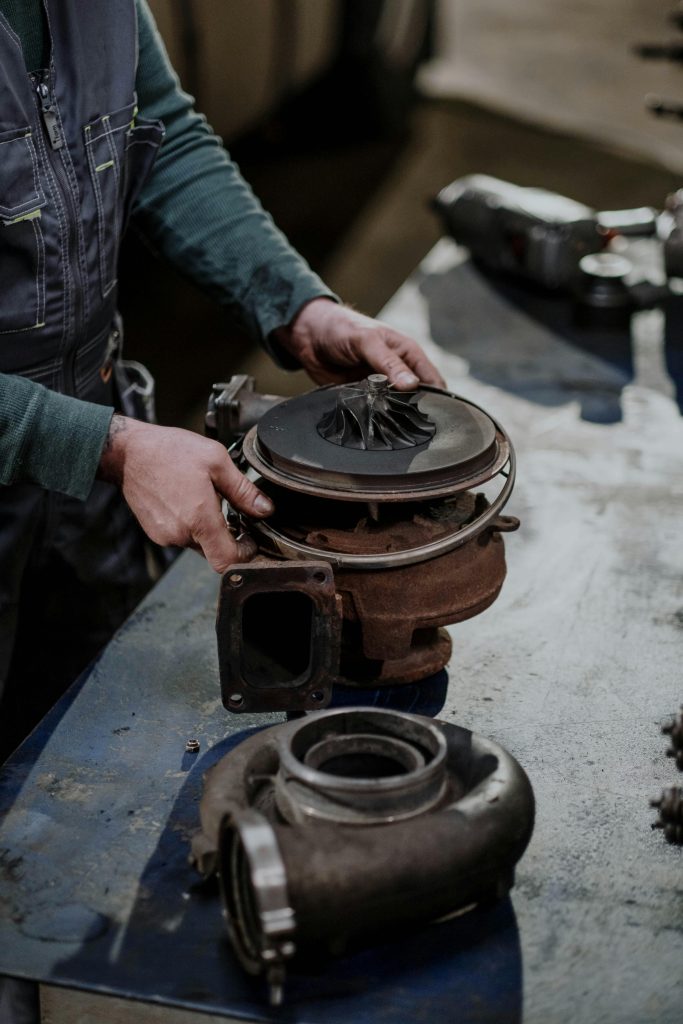 pexels-photo-7565170-7565170 Mechanic working on a turbocharger assembly in a repair shop setting.